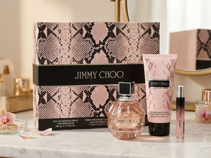Jimmy Choo Eau De Parfum Gift Set with a 100ml faceted bottle, 100ml Body Lotion, 7.5ml travel spray, and pink python-print gift box on a marble vanity